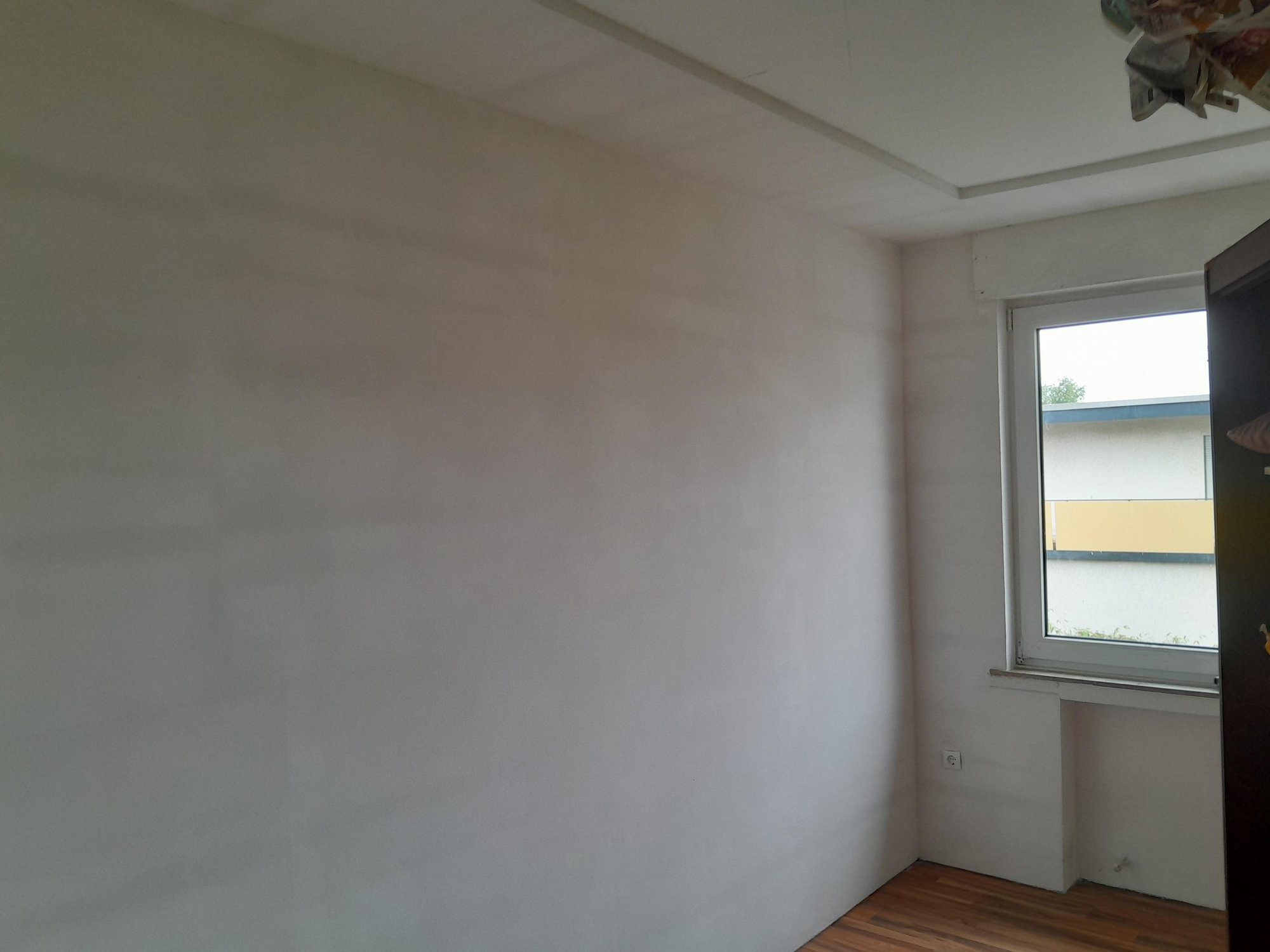 Leerer Raum mit weißer Wand, Fenster und Holzfußboden, Blick in eine Ecke.