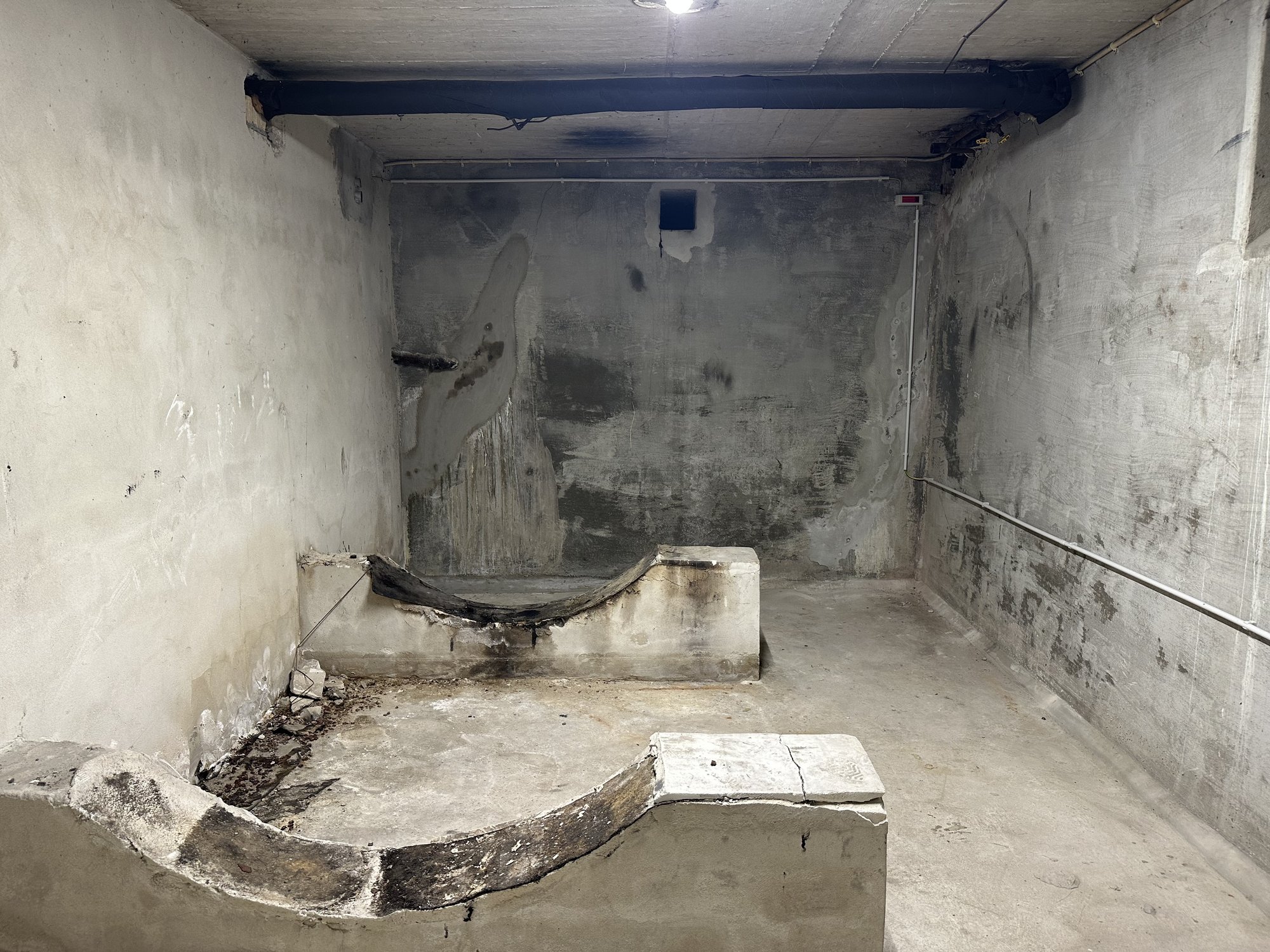 Unfertiger Betonkellerraum mit dunklen Feuchteflecken an der Kellerwand und beschädigter Betonstufe.