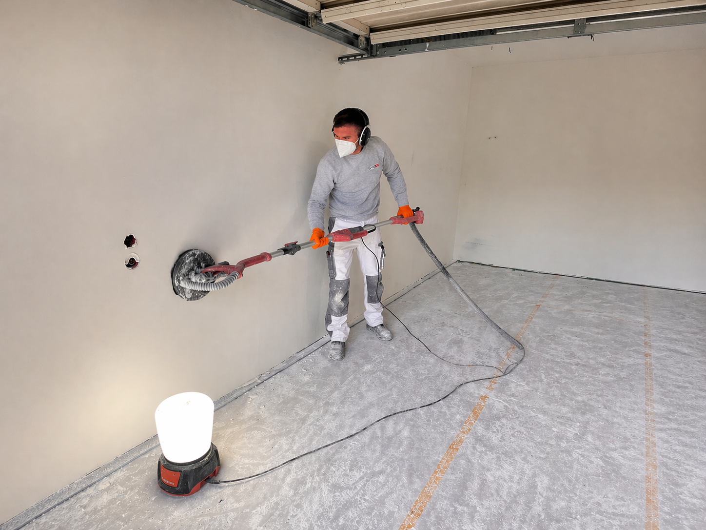 ISOTEC Mitarbeiter schleift Wand mit Langhalsschleifer und Absaugschlauch im leeren Raum