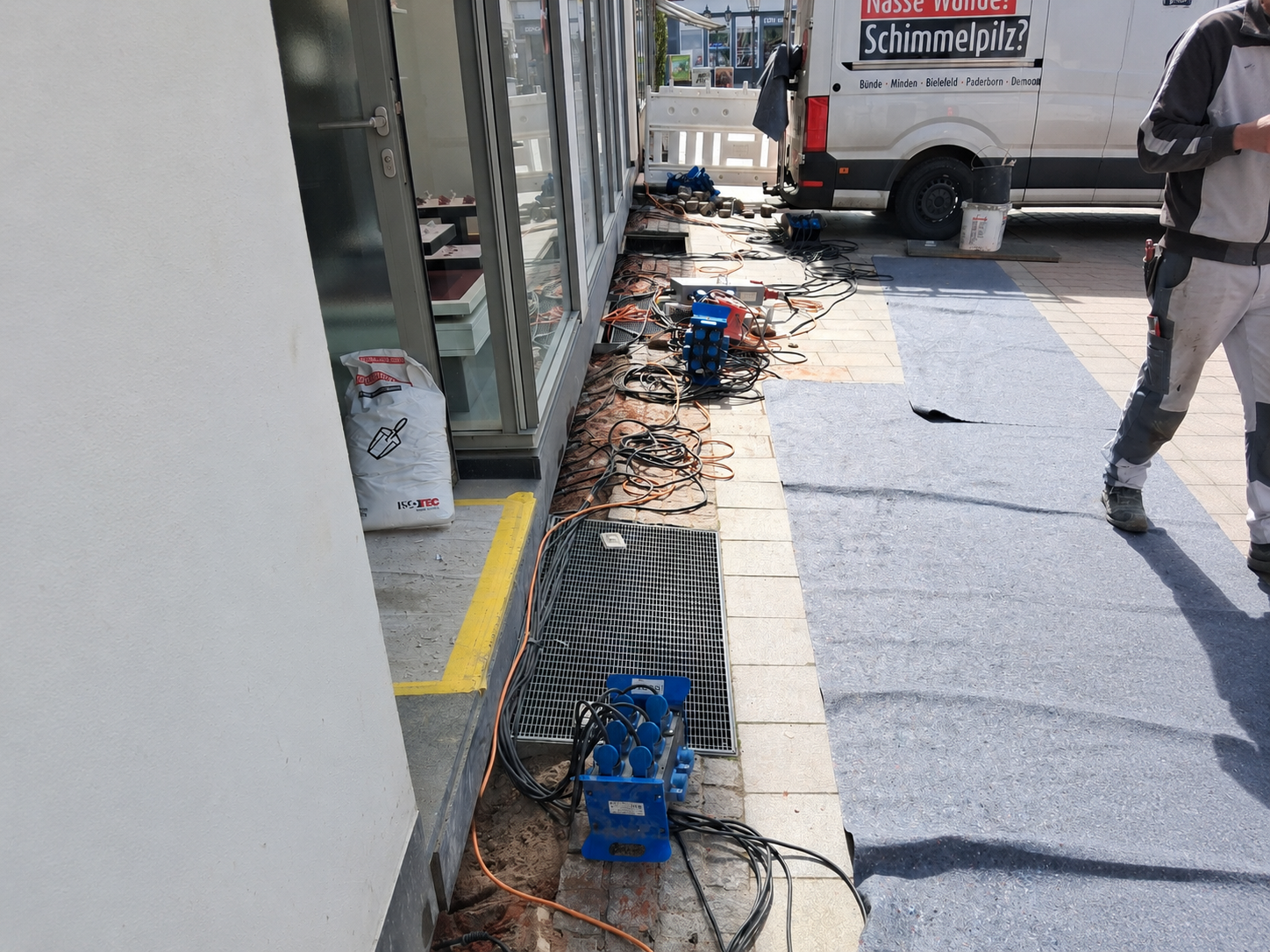 ISOTEC Baustelle mit Kabeln, Stromverteilern und Schutzvlies am Gehweg vor Glasfront
