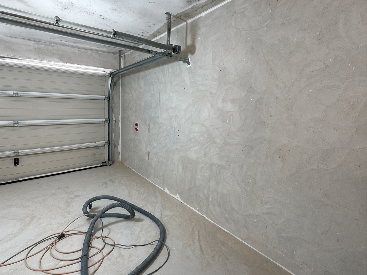 Garage mit grauer Wandoberflaeche, Garagentor und Schlaeuchen am Boden