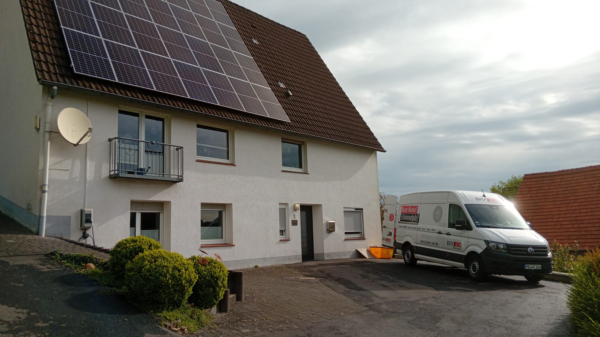 ISOTEC Transporter vor Wohnhaus mit Solaranlage auf dem Dach, Einfahrt bei bewölktem Himmel