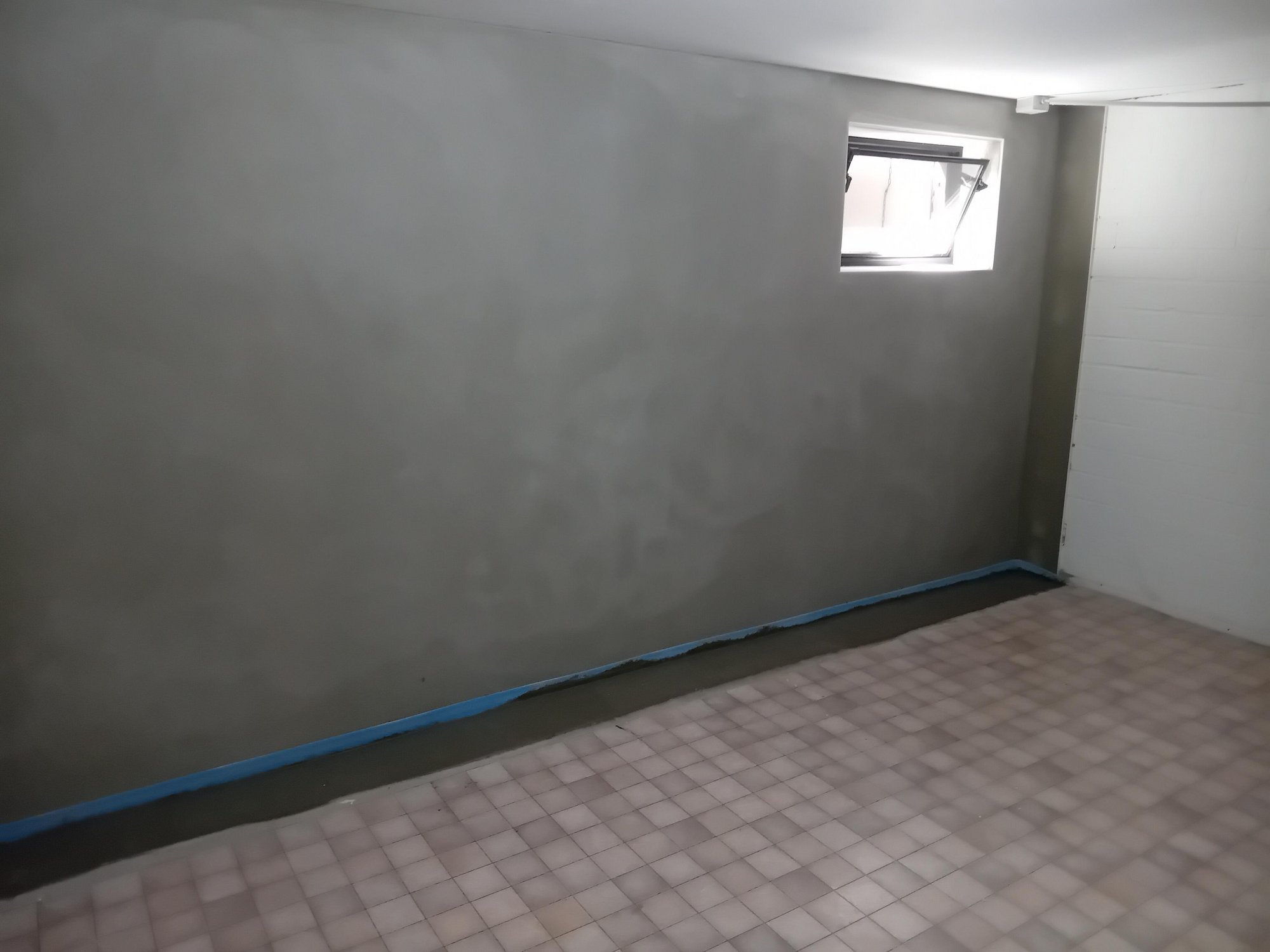 Wand mit grauer Masse bestrichen, Bodenkante mit blauem Klebeband abgeklebt