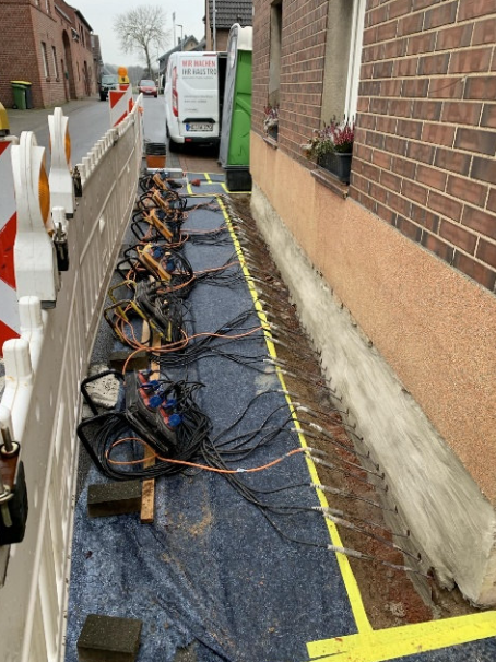 Kabel und Schläuche auf abgedecktem Gehweg neben Hausfassade