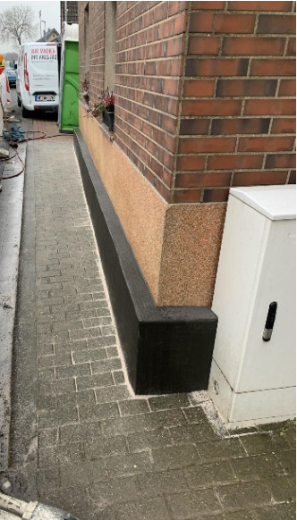 Schwarze Masse am Sockel einer Ziegelhauswand, Gehwegansicht