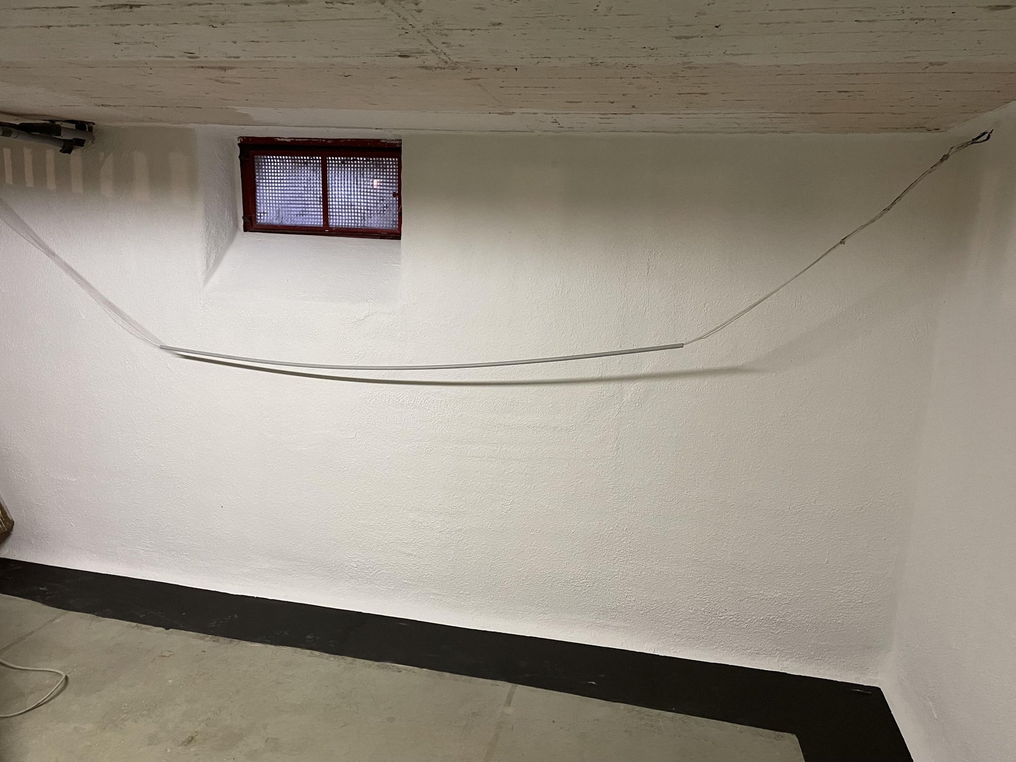 Weiße Kellerwand mit kleinem Fenster und gespanntem Kabel.