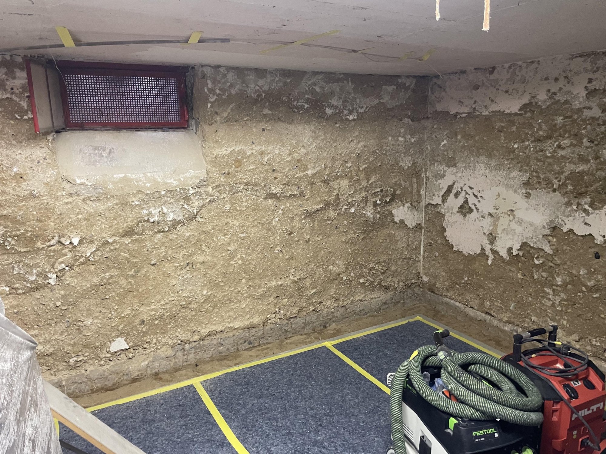 Beschädigte Kellerwand mit bröckelnder Oberfläche und Geräten im Vordergrund