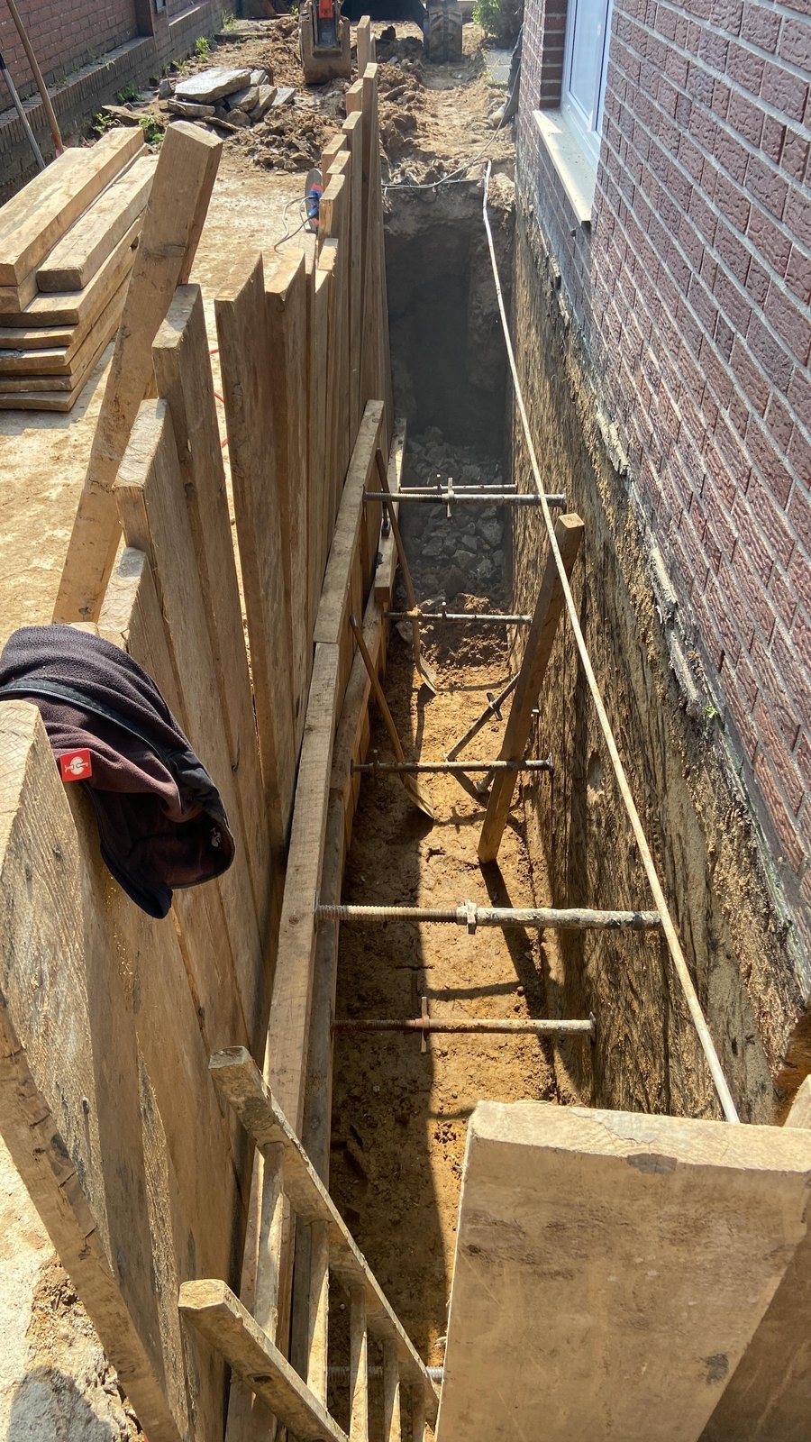 Tiefer Baugraben mit Holzverbau entlang einer Ziegelwand am Haus.