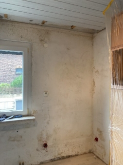 Leere Zimmerecke mit fleckiger Wand und offenem Fenster