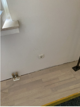 Weiße Wand mit Steckdose über hellem Holzboden, leere Zimmerecke