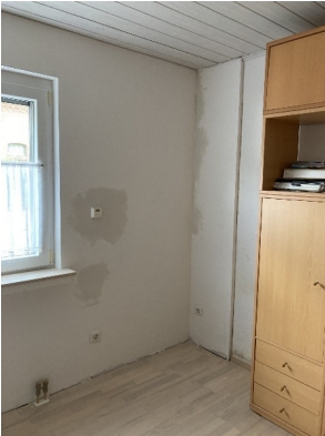 Helles Zimmer mit verfärbter Wand neben Fenster und Holzschrank