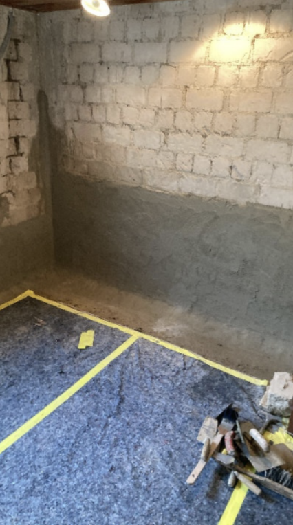Graue Masse auf Steinwand aufgetragen, Boden mit blauem Vlies abgedeckt und Werkzeug liegt bereit