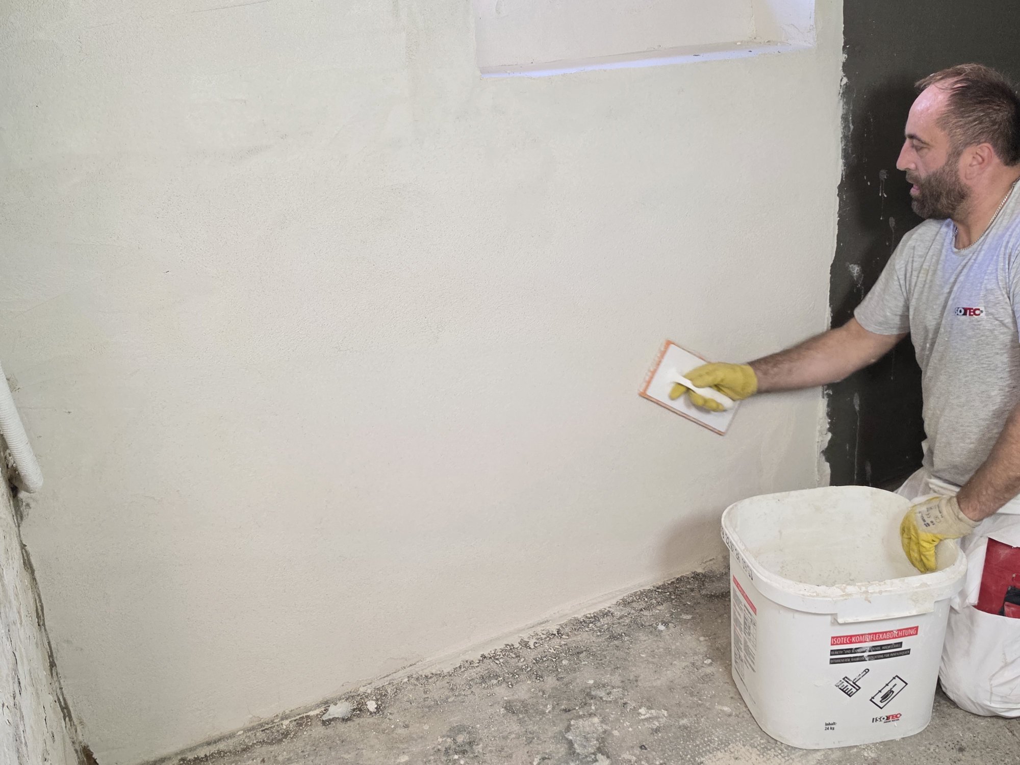 ISOTEC Mitarbeiter glättet helle Masse auf Kellerwand