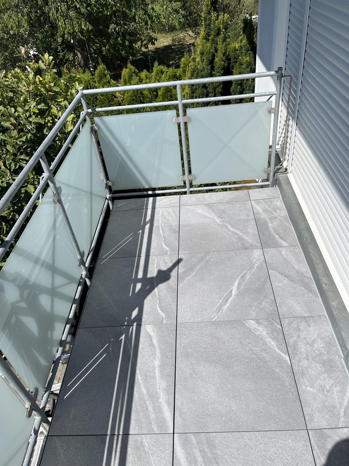 Balkon mit grauen Fliesen, Metallgeländer und satinierten Glaselementen