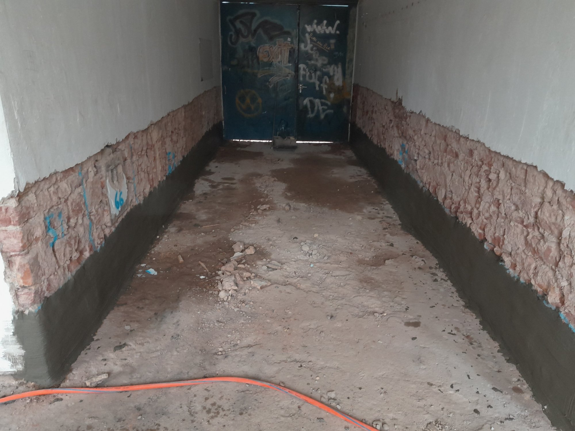 Freigelegte Wände mit aufgetragener grauer Masse in schmalem Raum