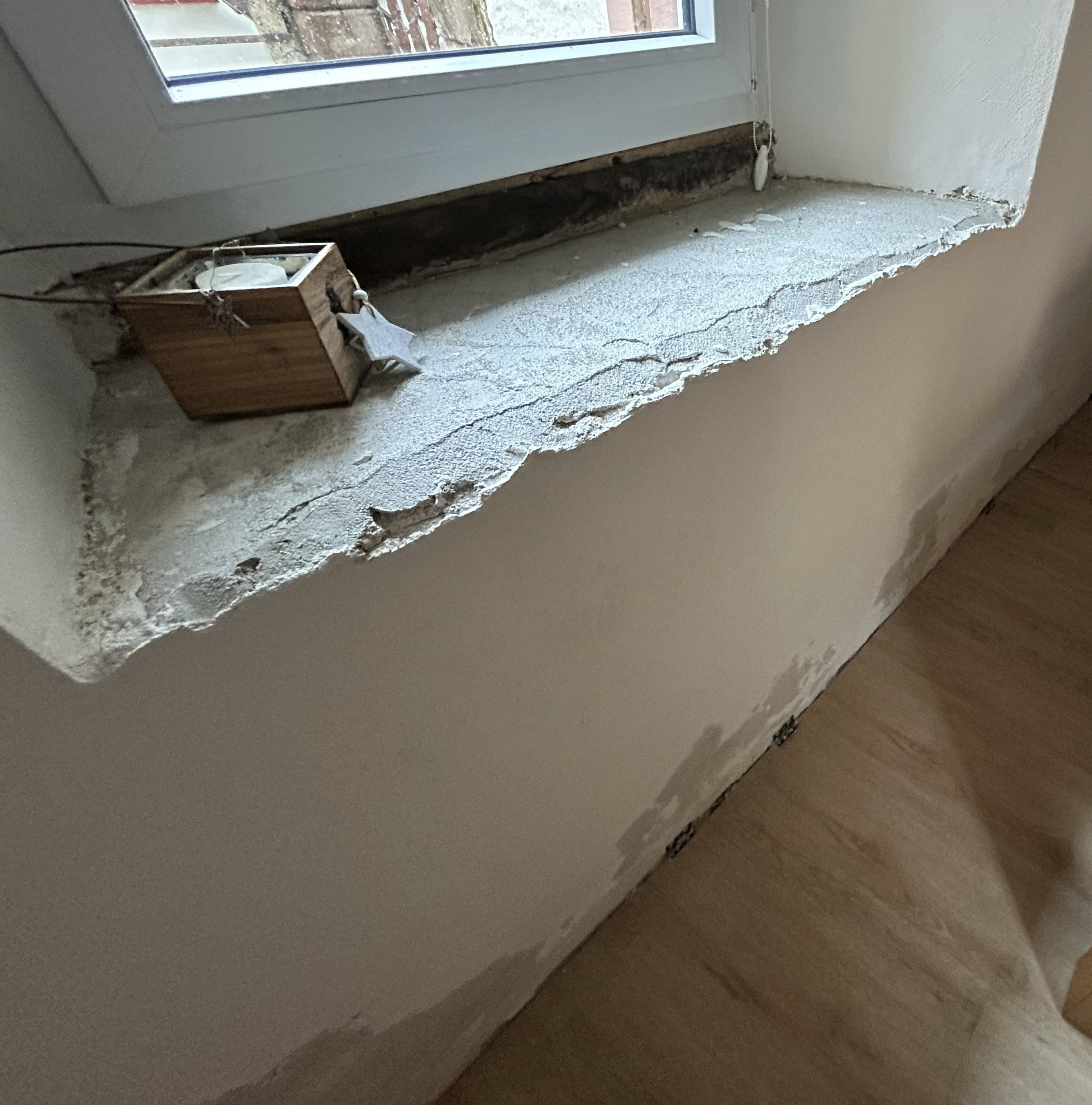 Beschädigte Fensterlaibung mit bröckelnder grauer Oberfläche.