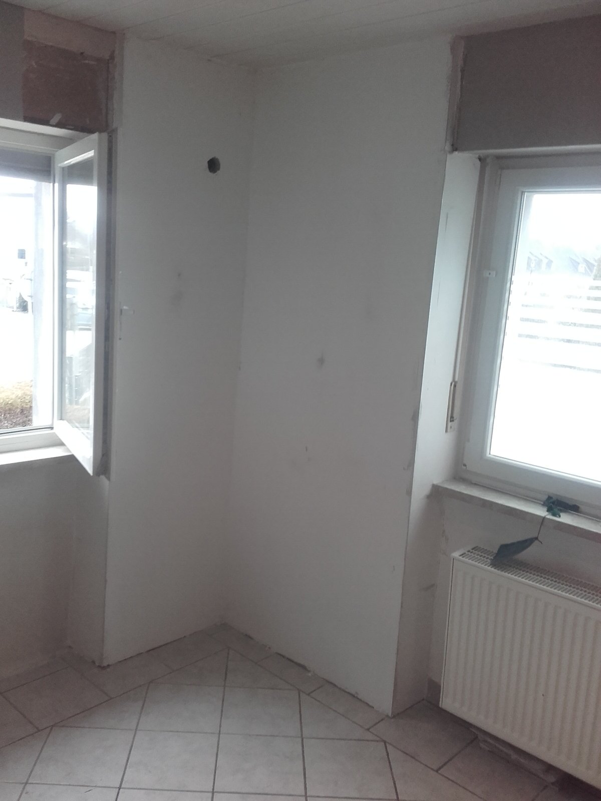 Helle Zimmerecke mit weißer Wand, zwei Fenstern und kleiner Öffnung