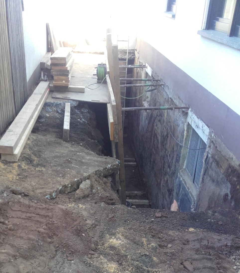 Aushubgraben entlang Gebäudewand mit freigelegter Kellerwand und Abstützungen