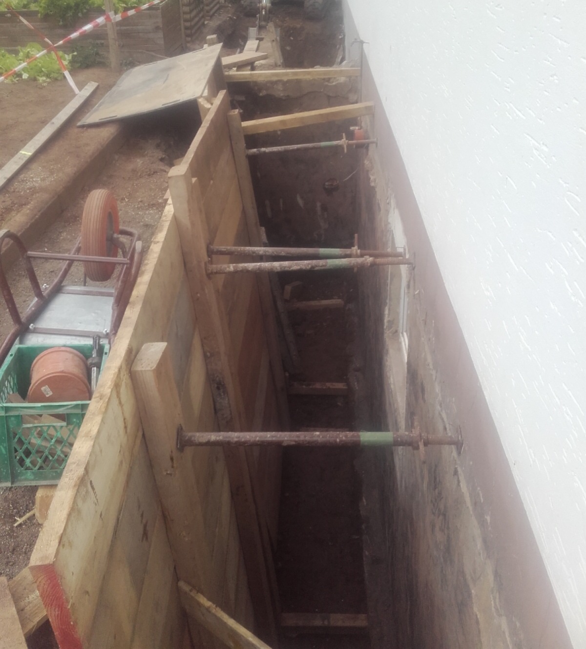 Offene Baugrube mit Holzabstützung entlang einer Gebäudewand