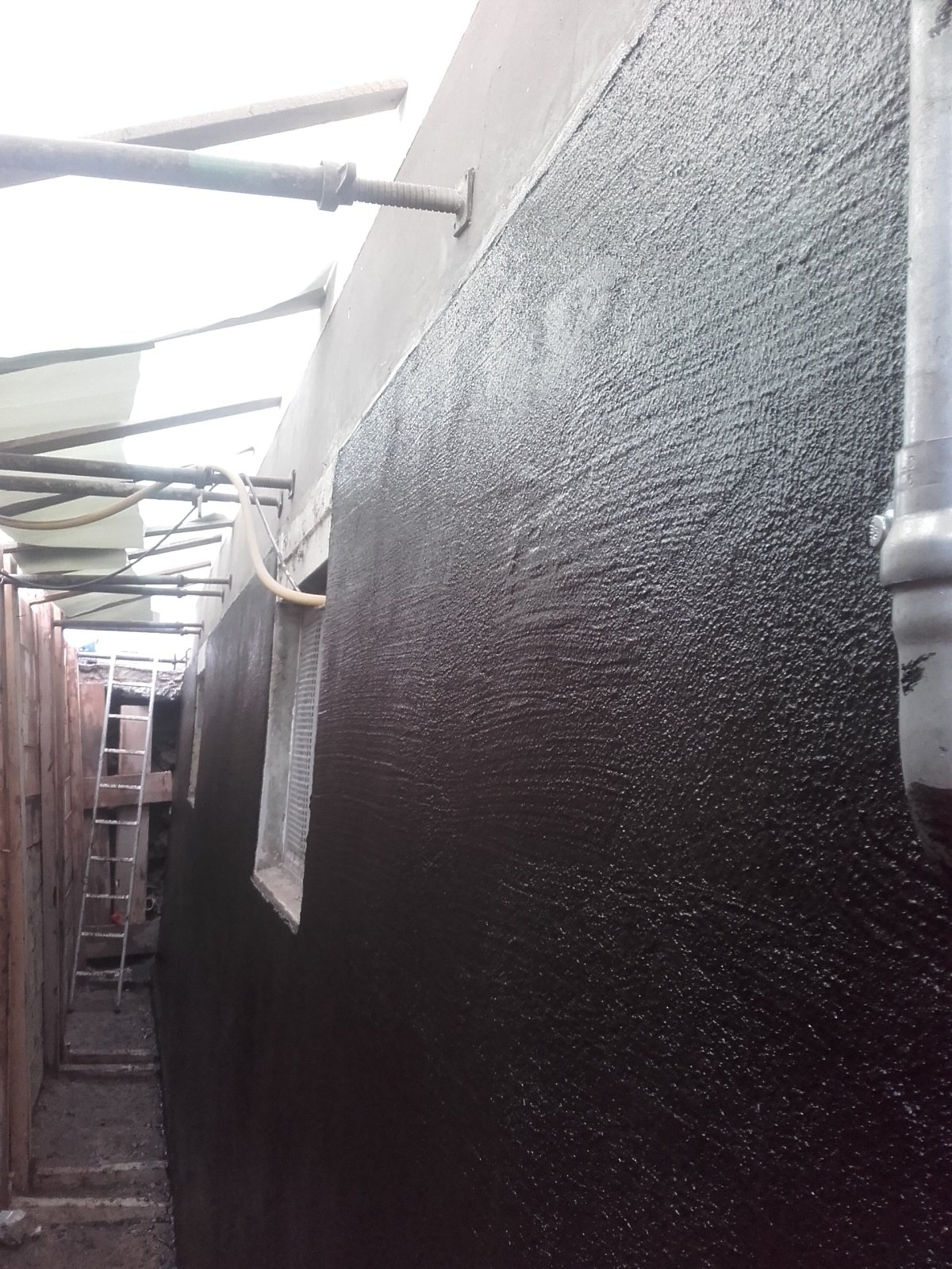 Schwarze Masse auf Kellerwand in schmalem Arbeitsgraben