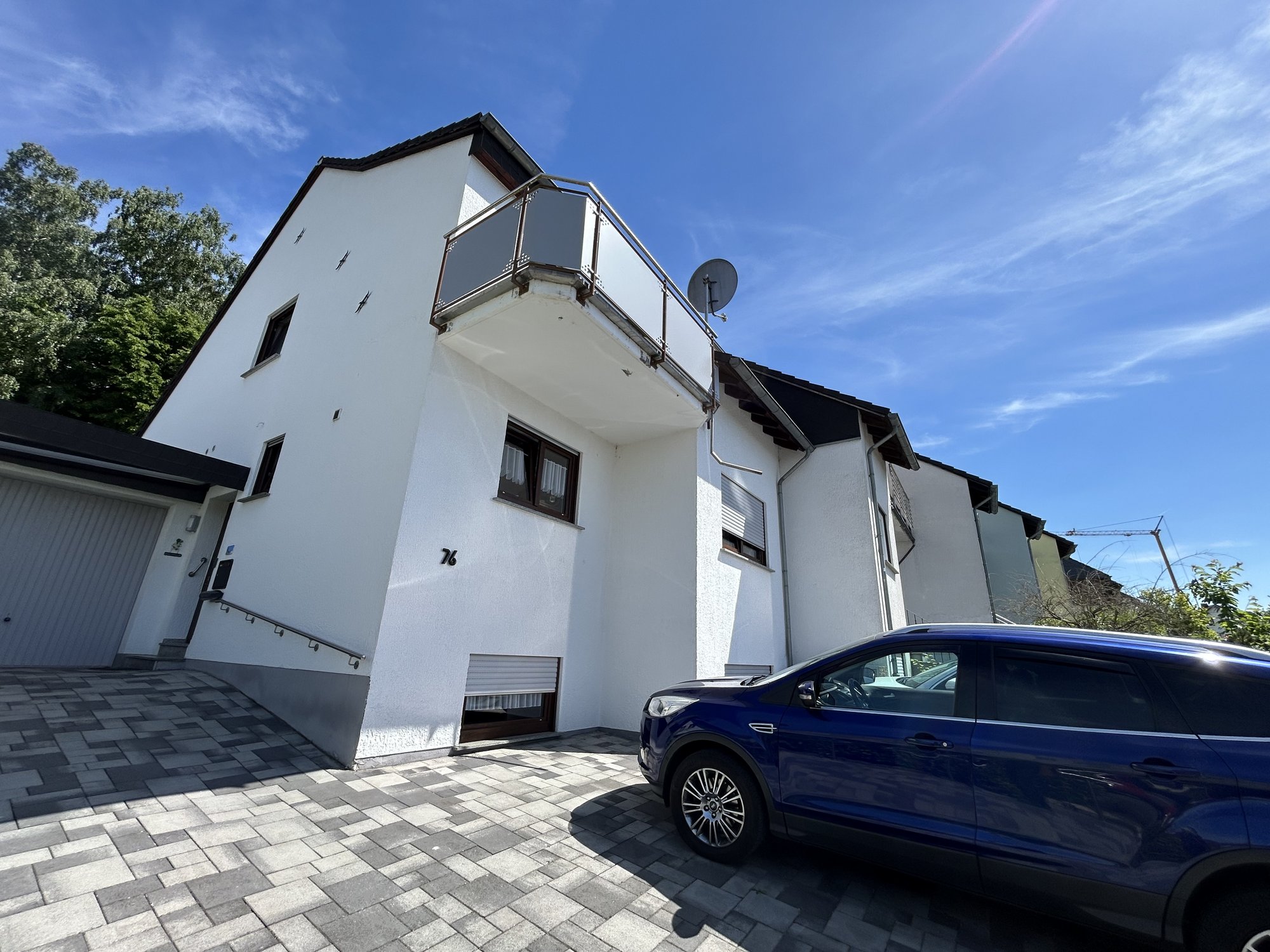 Weiße Gebäudefassade mit Balkon und geparktem Auto