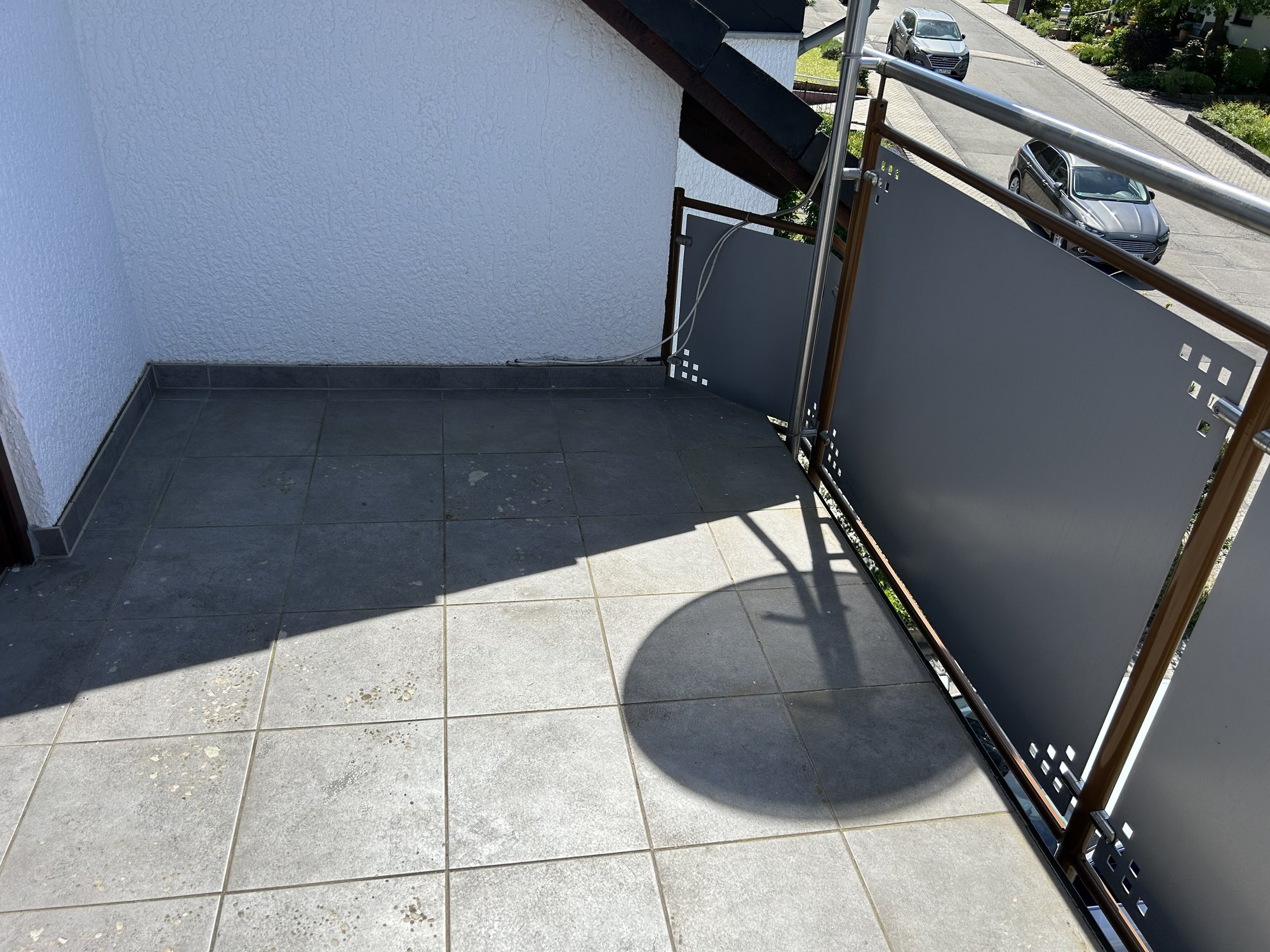 Sonniger Balkon mit grauen Fliesen und modernem Geländer