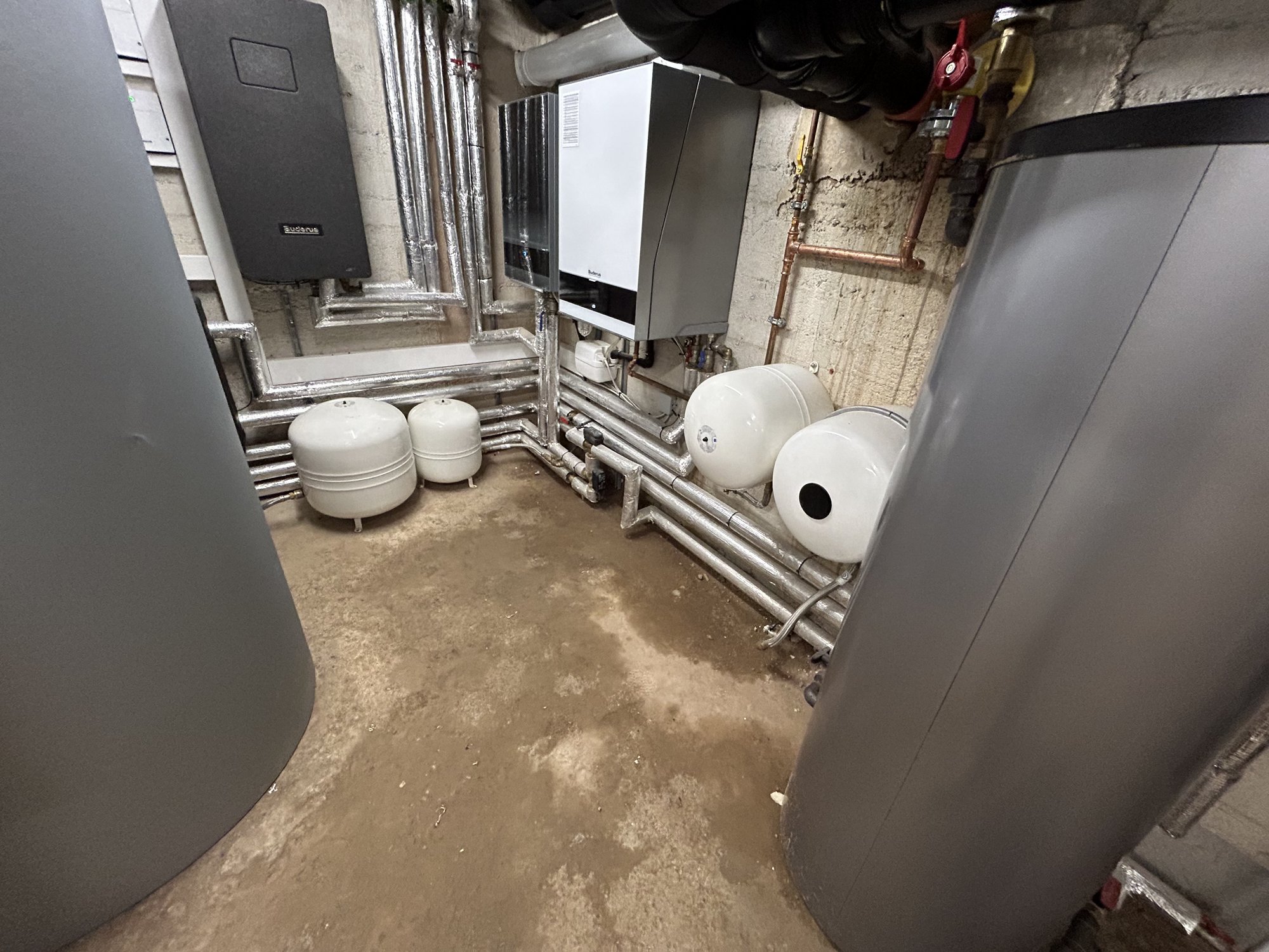 Technikraum mit grauen Behältern, weißen Drucktanks und isolierten Rohrleitungen.