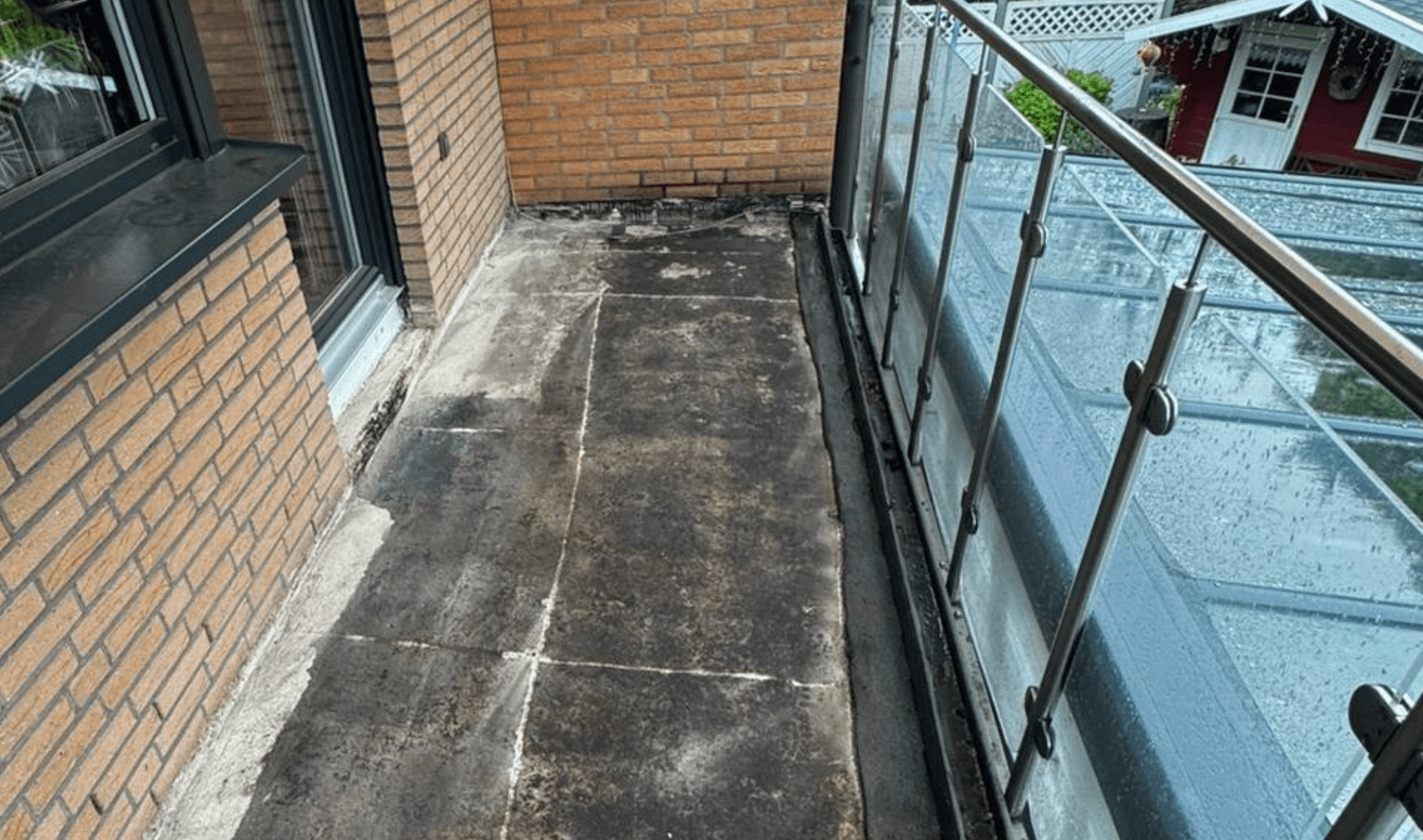Verschmutzter Balkonboden aus Platten neben Ziegelwand und Glasgeländer, Nahansicht