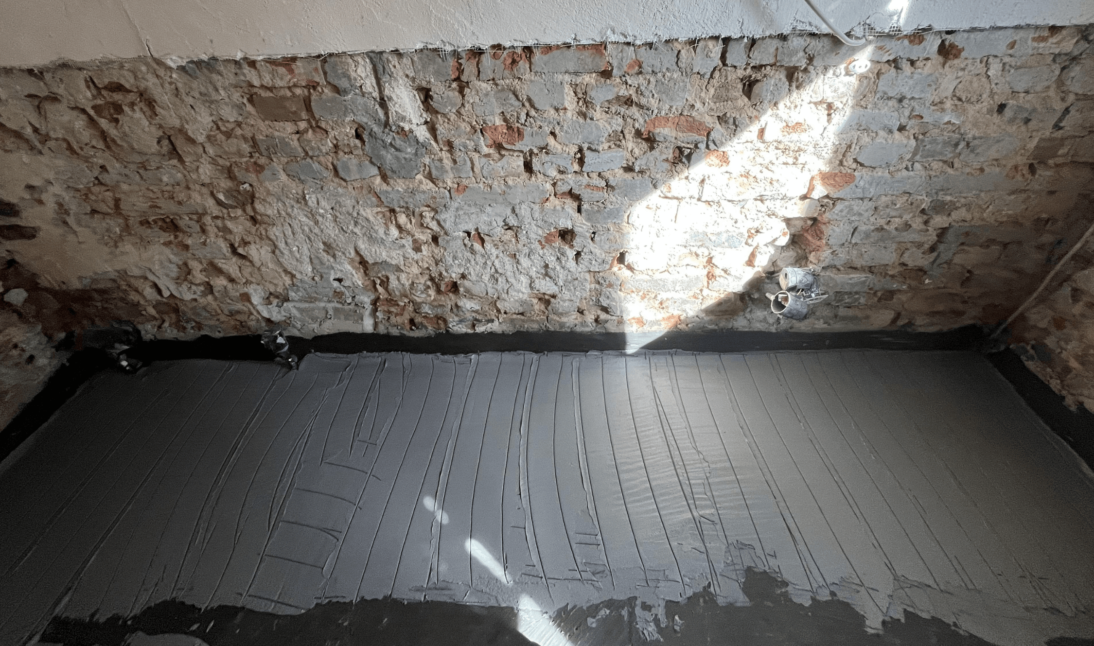 Freigelegte Ziegelwand mit grauen Mörtelresten, davor graue Folie auf dem Boden.