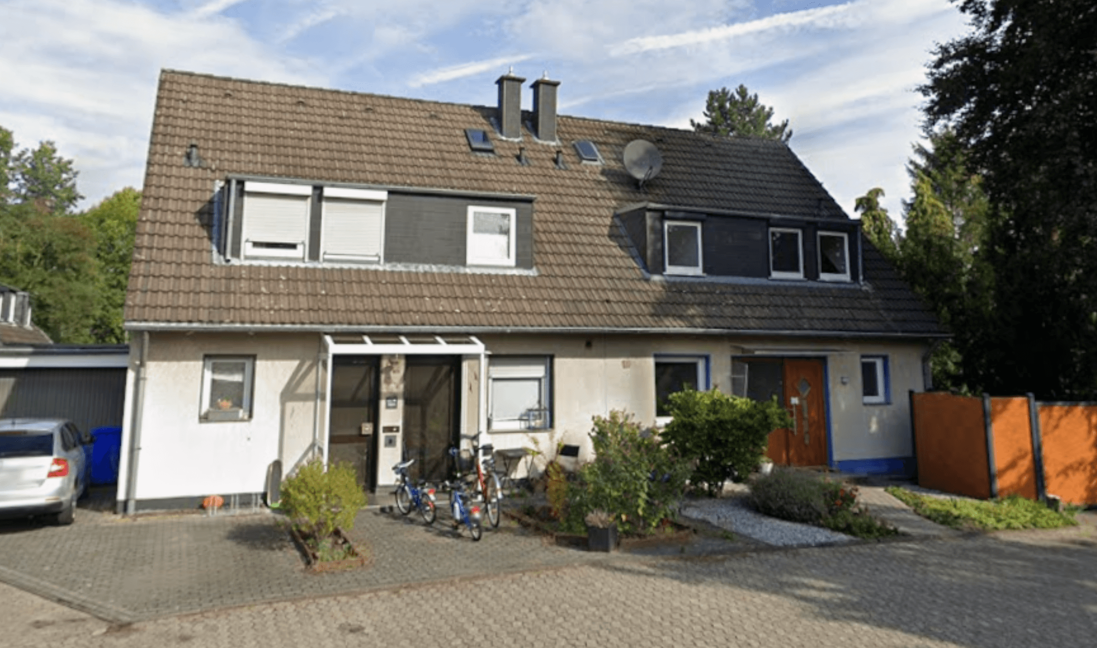 Mehrfamilienhaus mit geneigtem Ziegeldach, Dachgauben und gepflastertem Vorhof