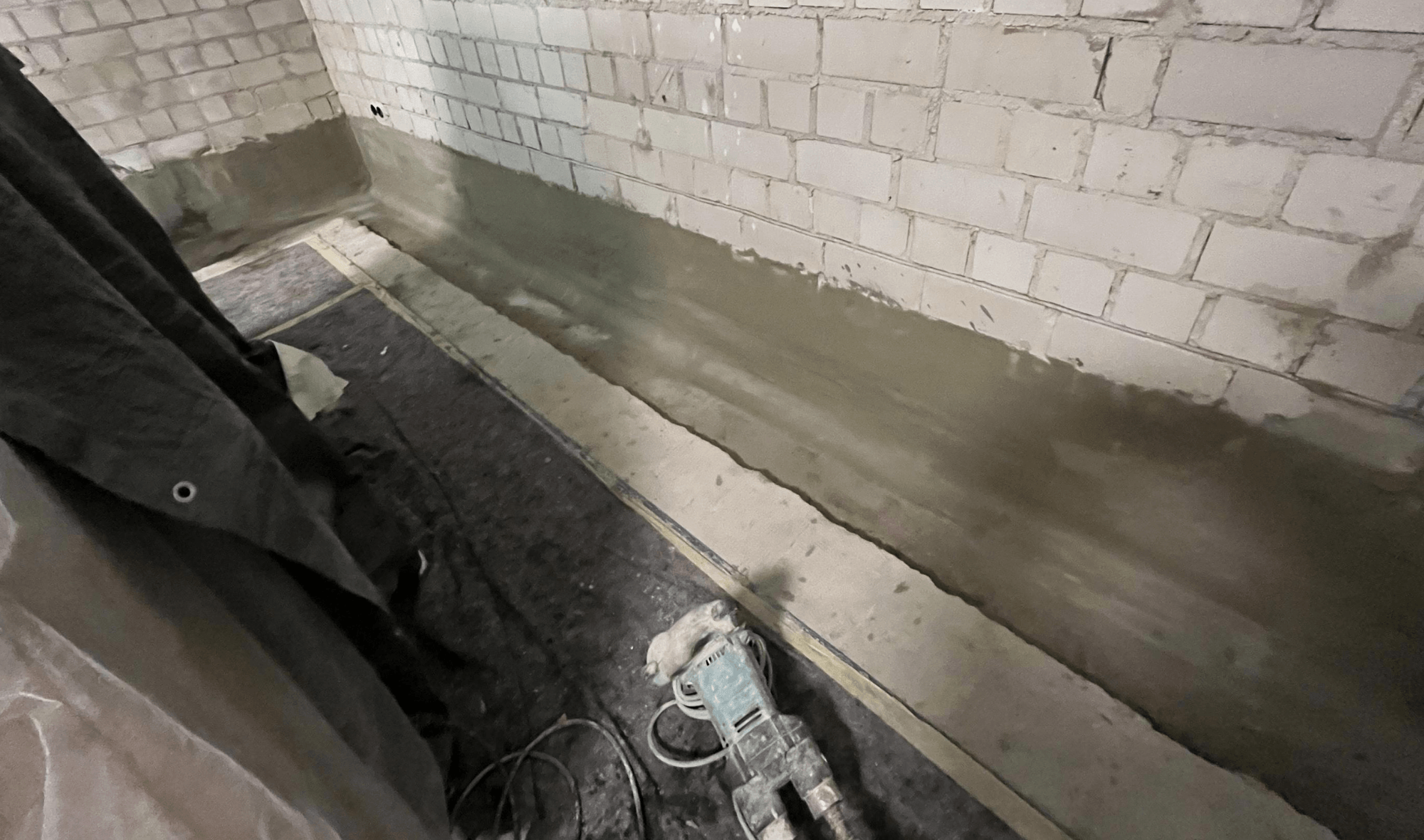 Graue Masse am Sockel einer Kellerwand aus weißen Ziegeln, Baustelle mit Abdeckvlies.