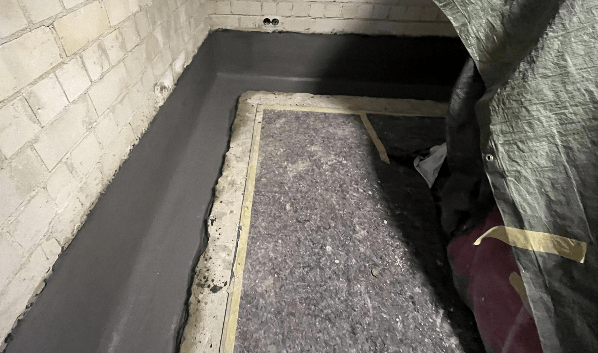 Graue Masse entlang der Boden-Wand-Fuge im Kellerraum, abgeklebt am Rand.
