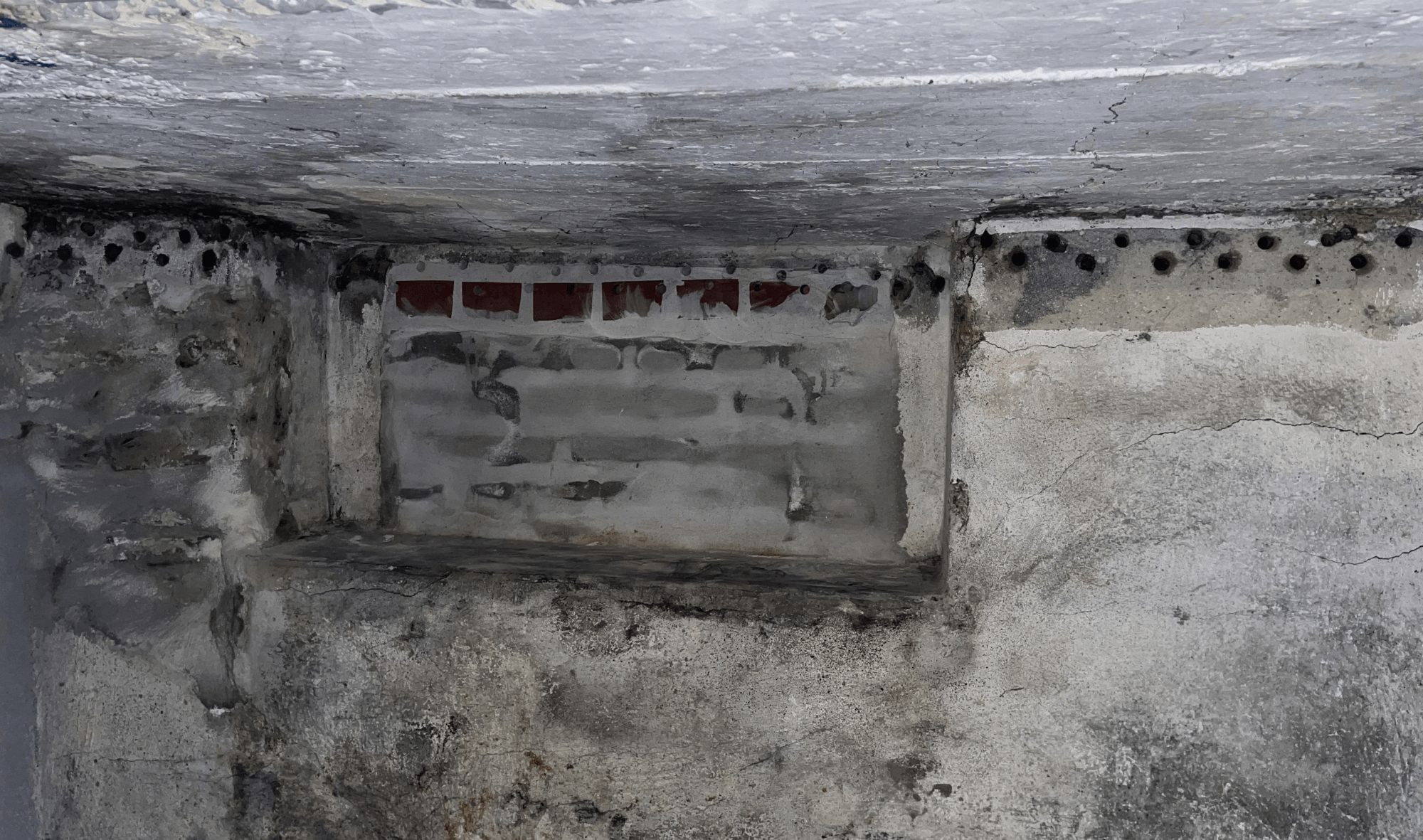 Bohrlochreihe über freigelegter Maueröffnung in Betonfläche, Risse sichtbar