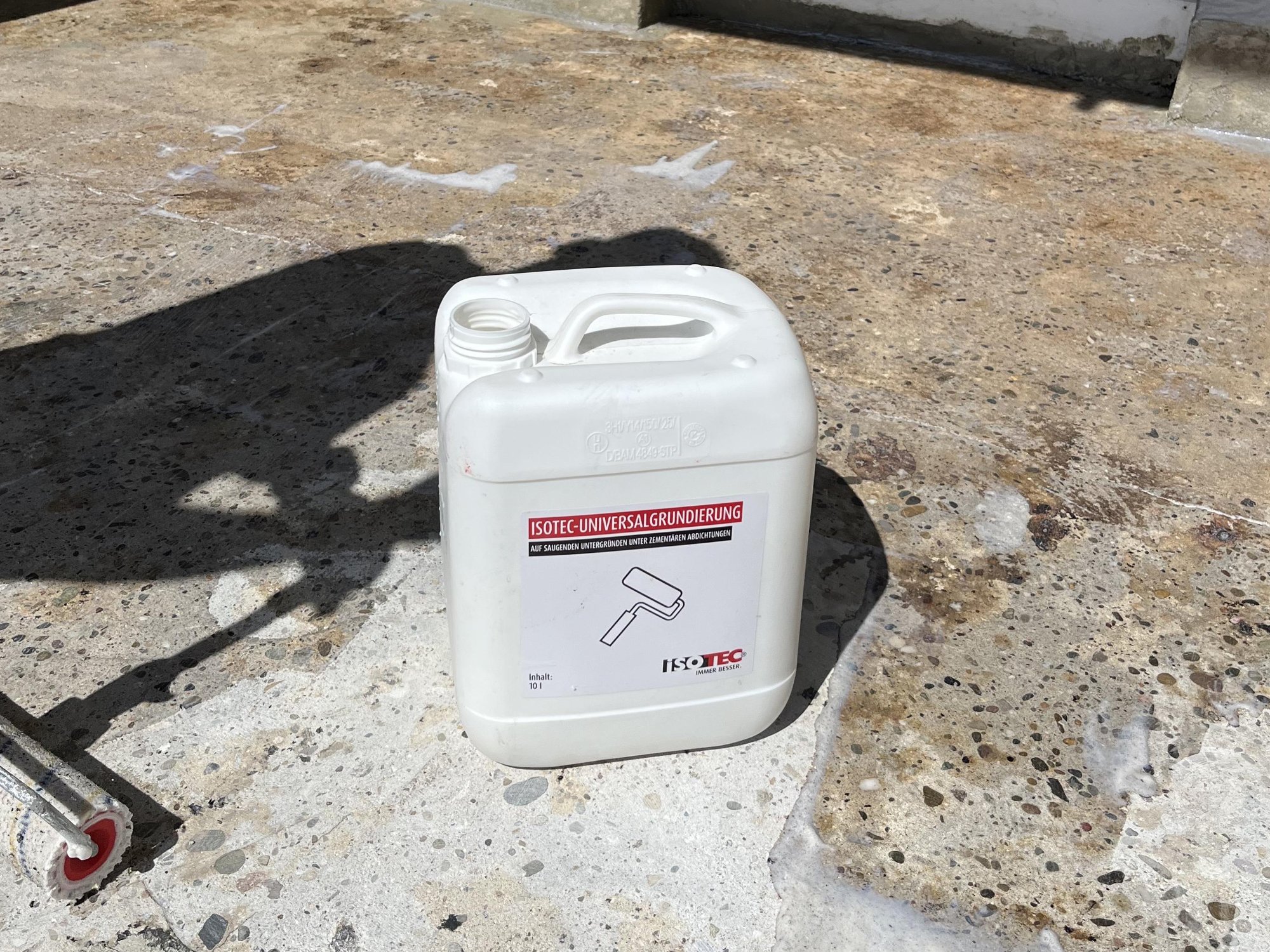 ISOTEC Kanister Universalgrundierung auf Betonboden neben Farbroller