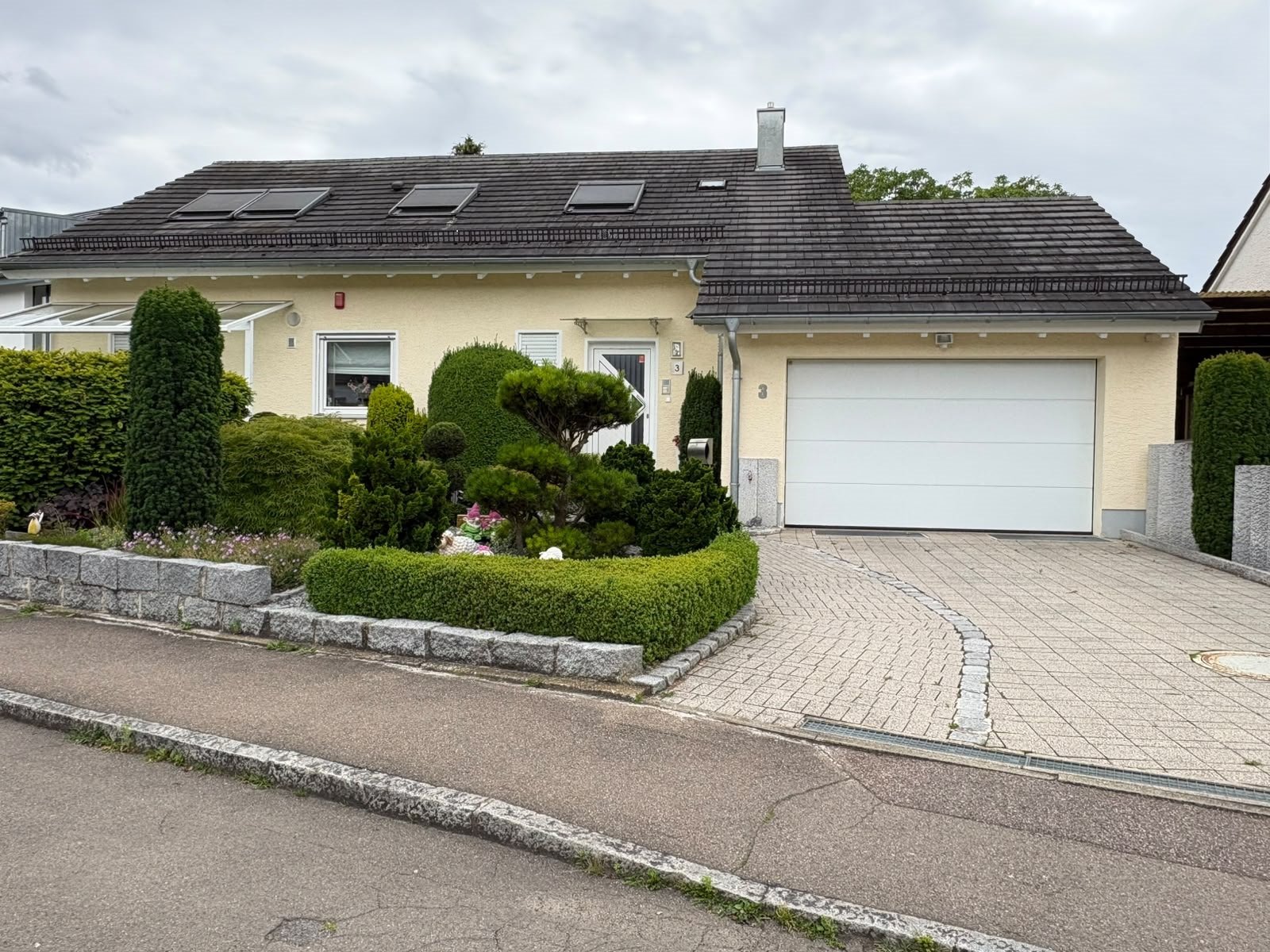 Einfamilienhaus mit Garage, dunklem Ziegeldach und gepflegtem Vorgarten an der Straße