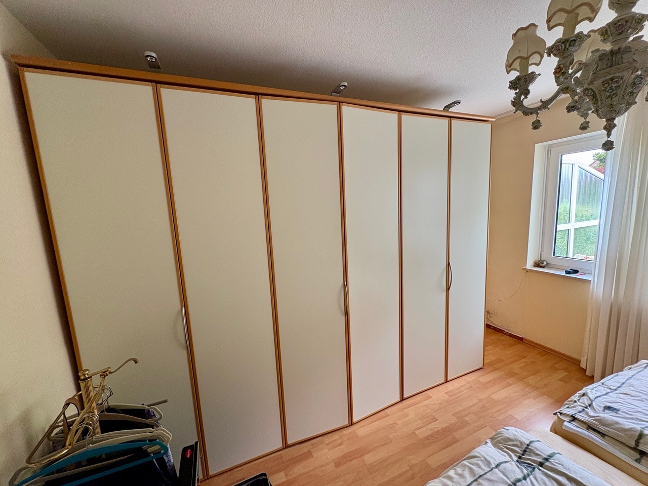 Großer weißer Kleiderschrank mit Holzrahmen in Zimmer, neben Fenster und Kronleuchter.