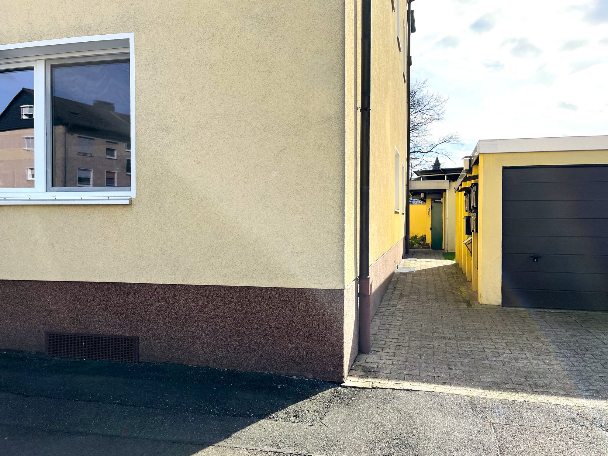 Helle Hausfassade mit Fenster, gepflasterter Einfahrt und Garage