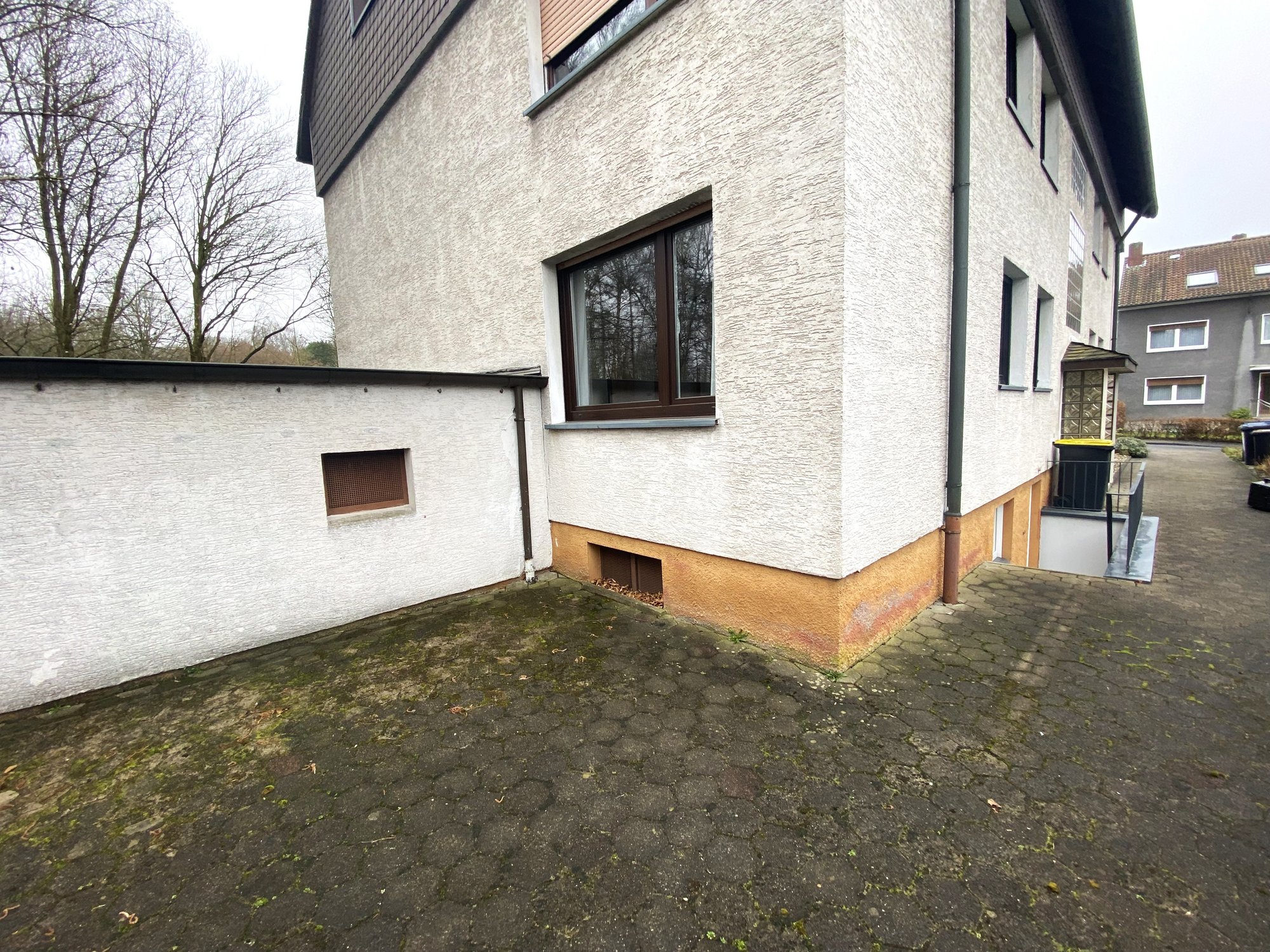 Gebäudeecke mit heller Fassade, Fallrohr und Hofbereich