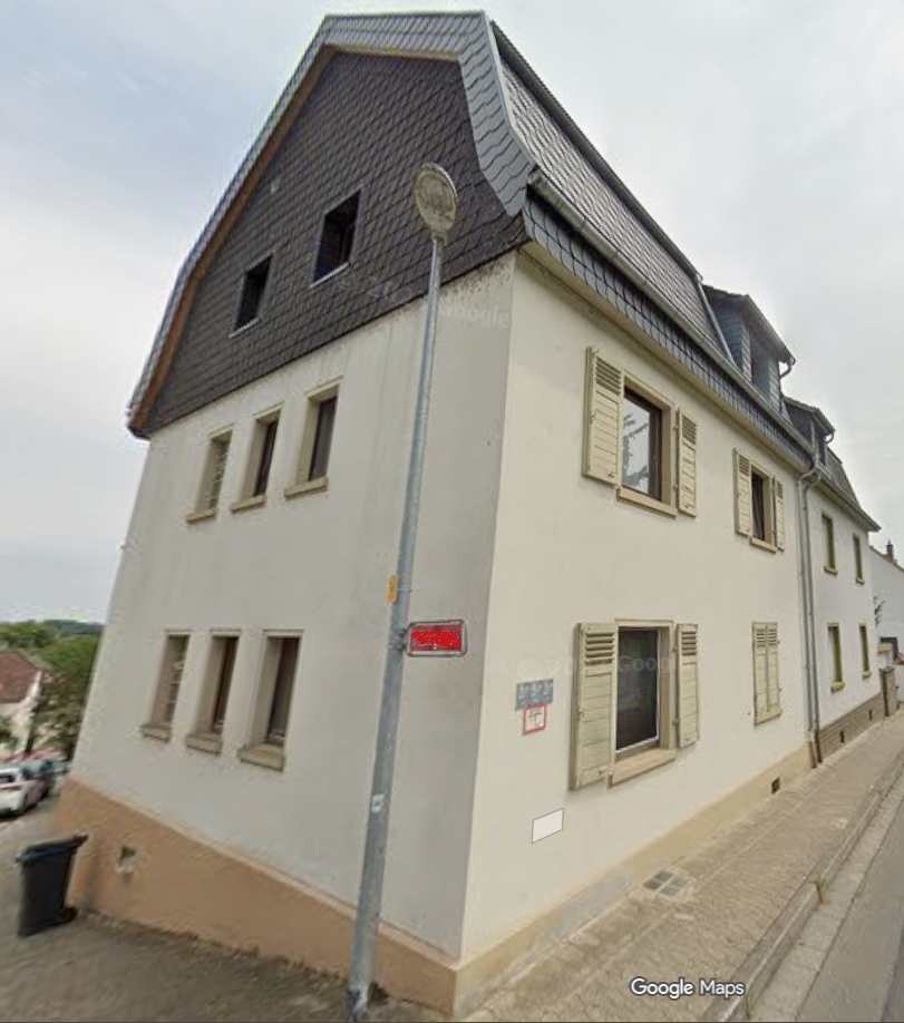 Straßenansicht eines mehrstöckigen Hauses mit Schieferdach und hellen Fensterläden.