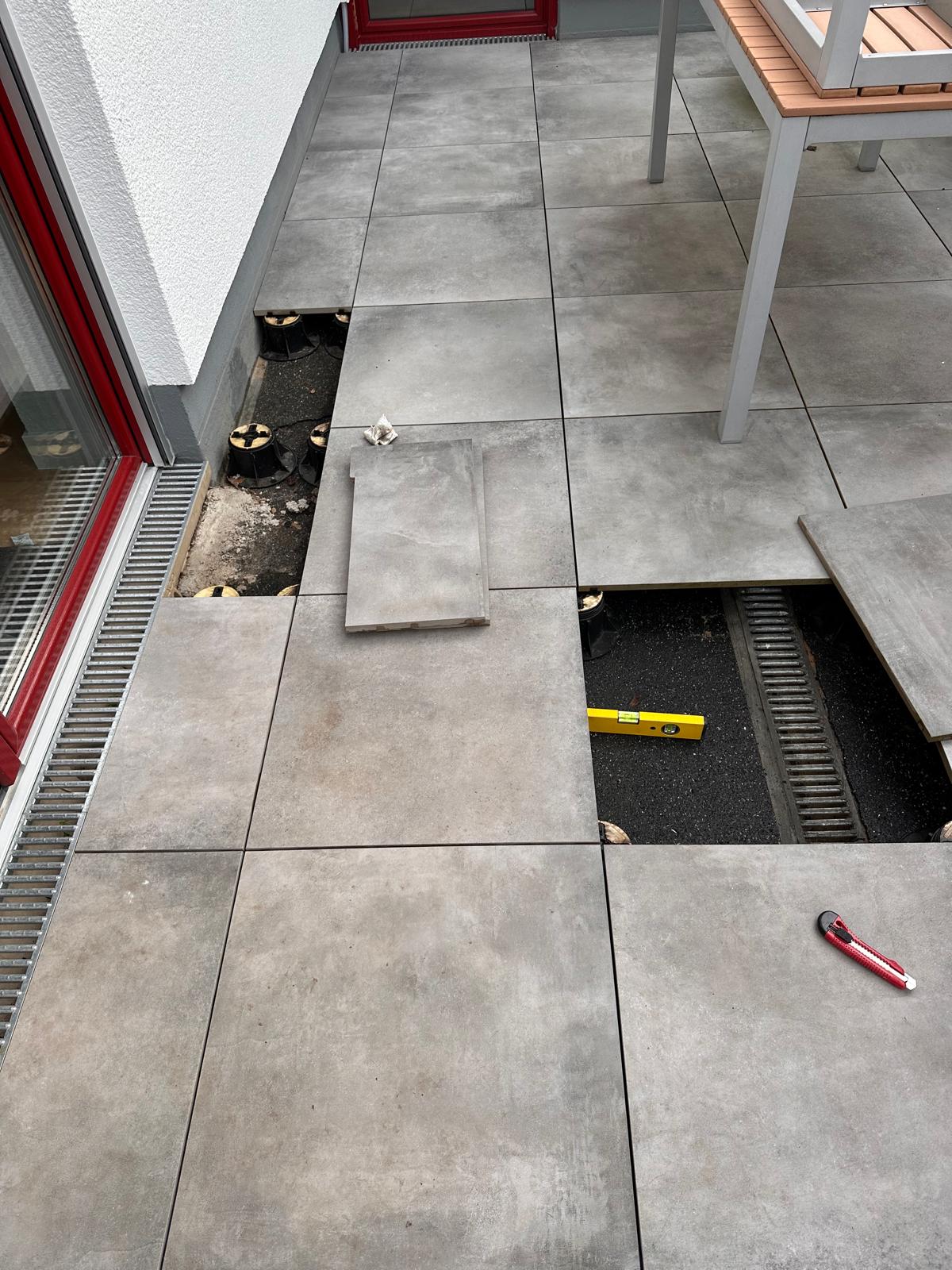 Verlegung grauer Terrassenplatten auf Stelzlagern, mit Wasserwaage und Cuttermesser