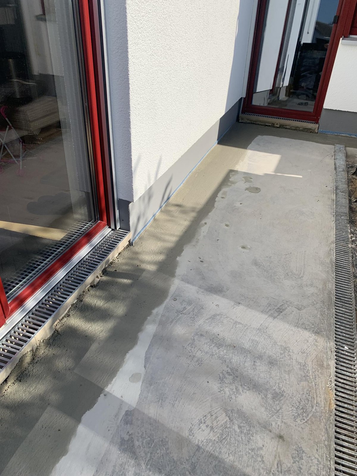 Balkonboden aus Beton mit grauer Beschichtung und Rinnenablauf neben Fenstertür