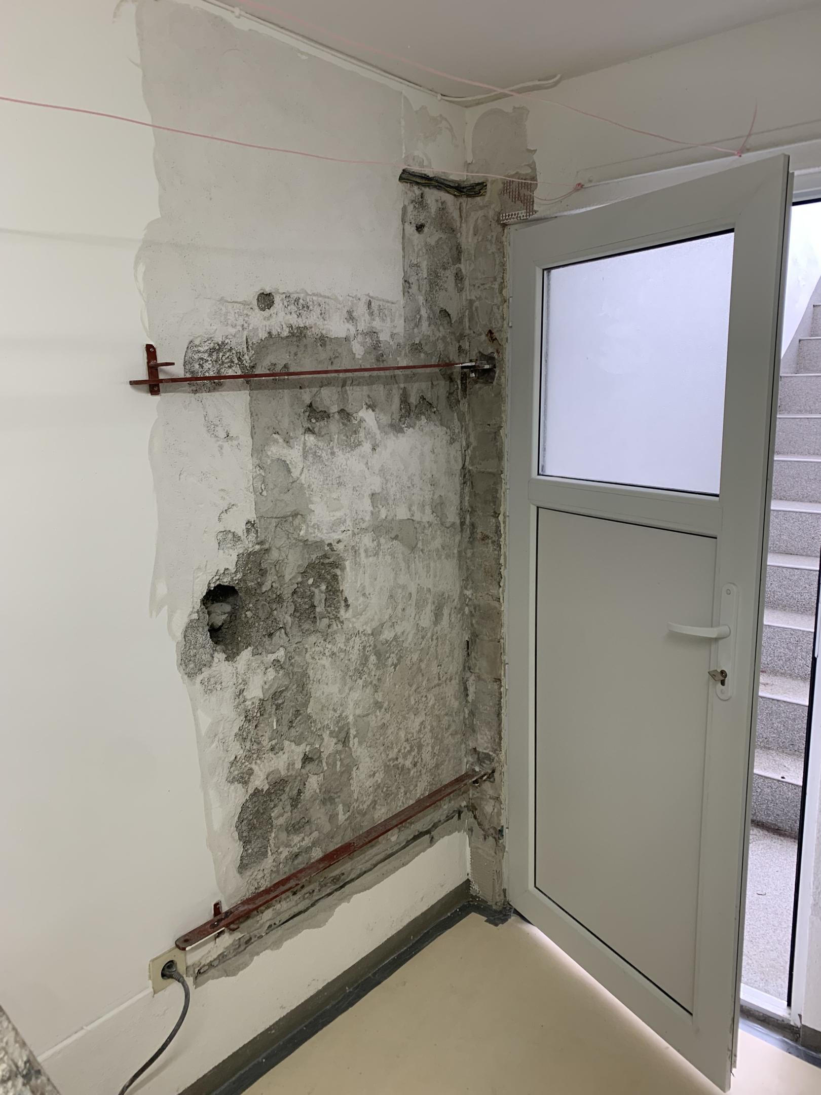 Abgeplatzter Wandputz mit dunklen Flecken neben Glastuer im Treppenhaus