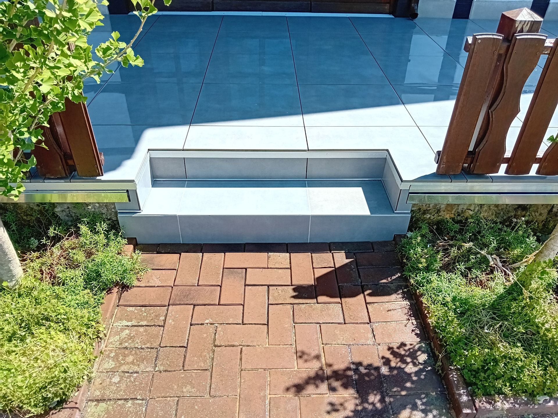 Geflieste Eingangsstufe vor Terrasse mit Holzgeländer und Pflasterweg
