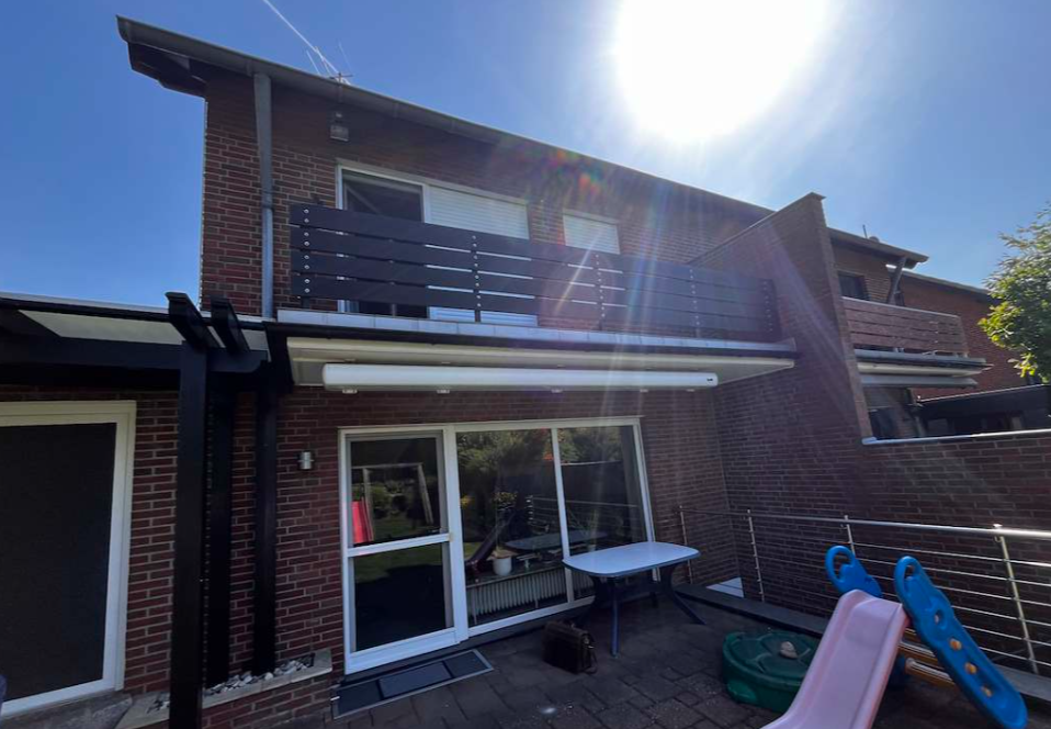 Backsteinhaus mit Balkon, Markise über Terrasse und Spielrutsche im Sonnenlicht