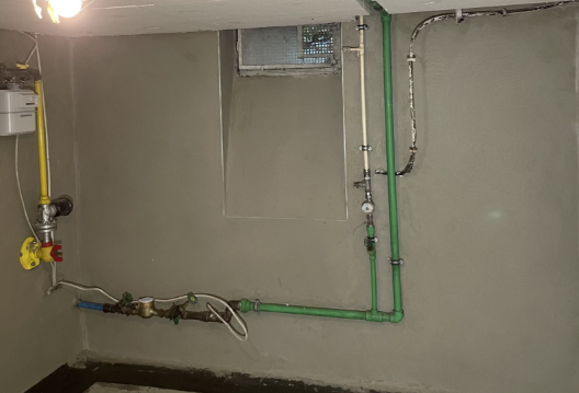 Kellerwand mit grünen und gelben Leitungen unter kleinem Fenster