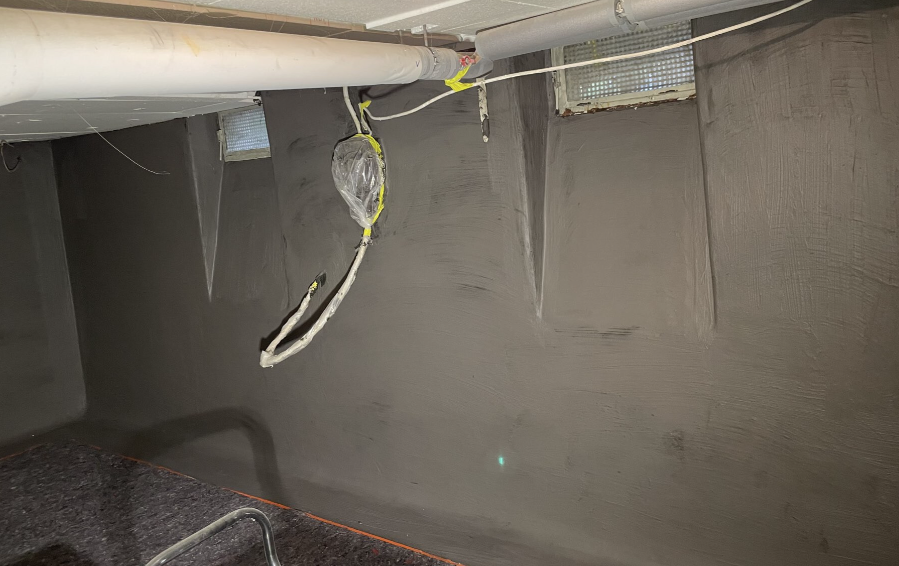 Dunkel beschichtete Kellerwand mit Leitungen und abgeklebten Kabeln