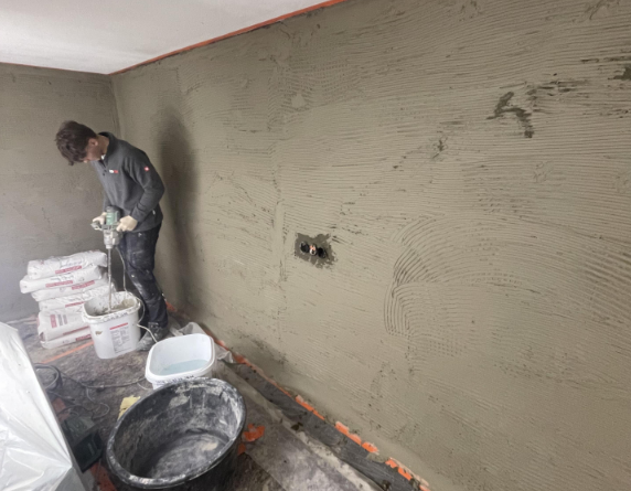 Mitarbeiter trägt graue Masse auf Zimmerwand auf