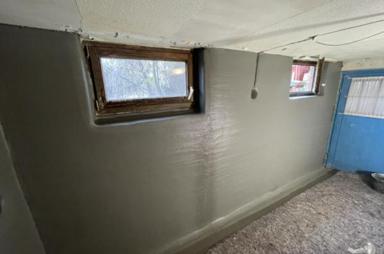 Graue beschichtete Kellerwand mit zwei kleinen Fenstern und blauer Tür