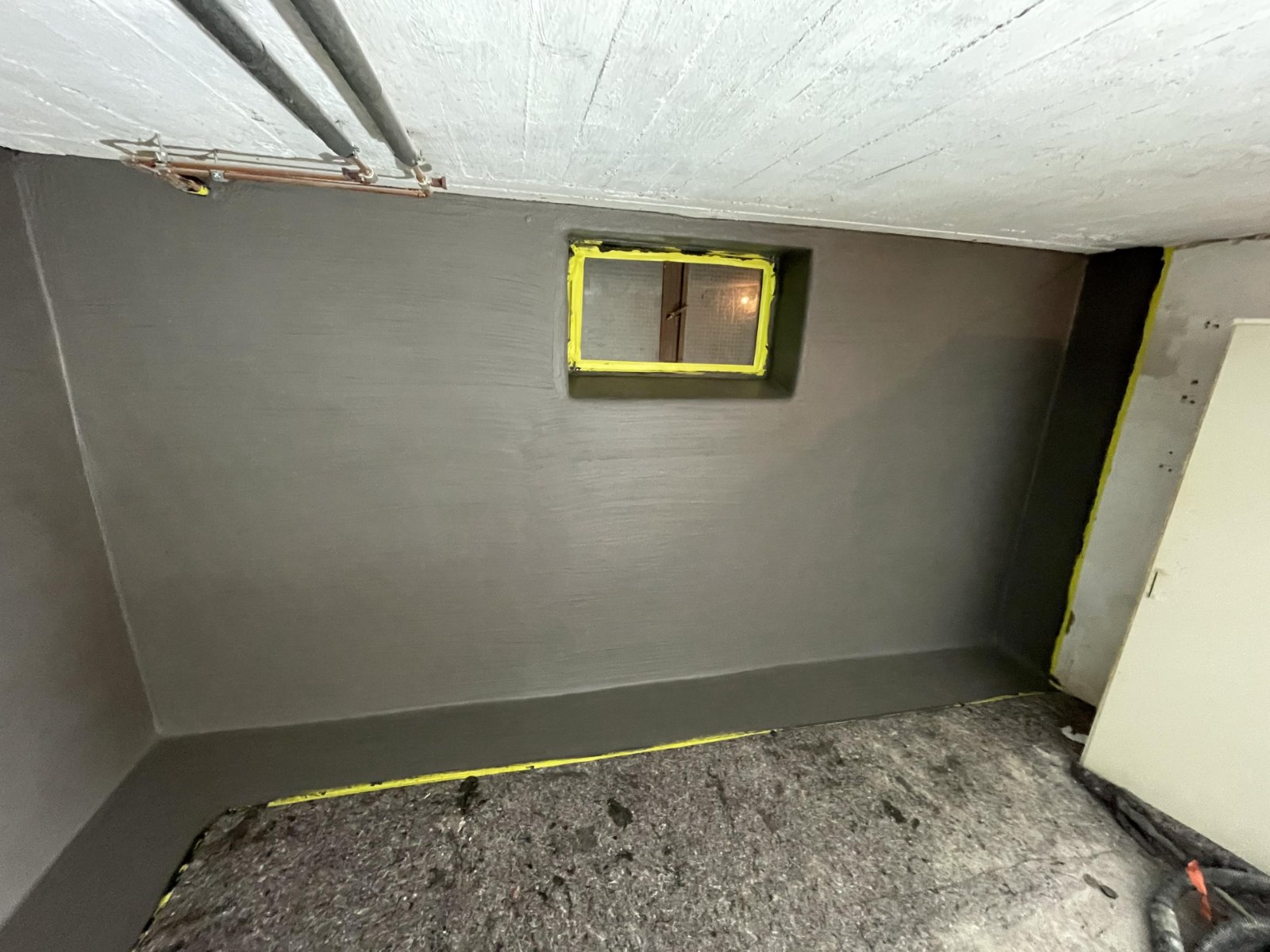 Kellerwand mit grauer Masse beschichtet, gelbes Klebeband am Fenster