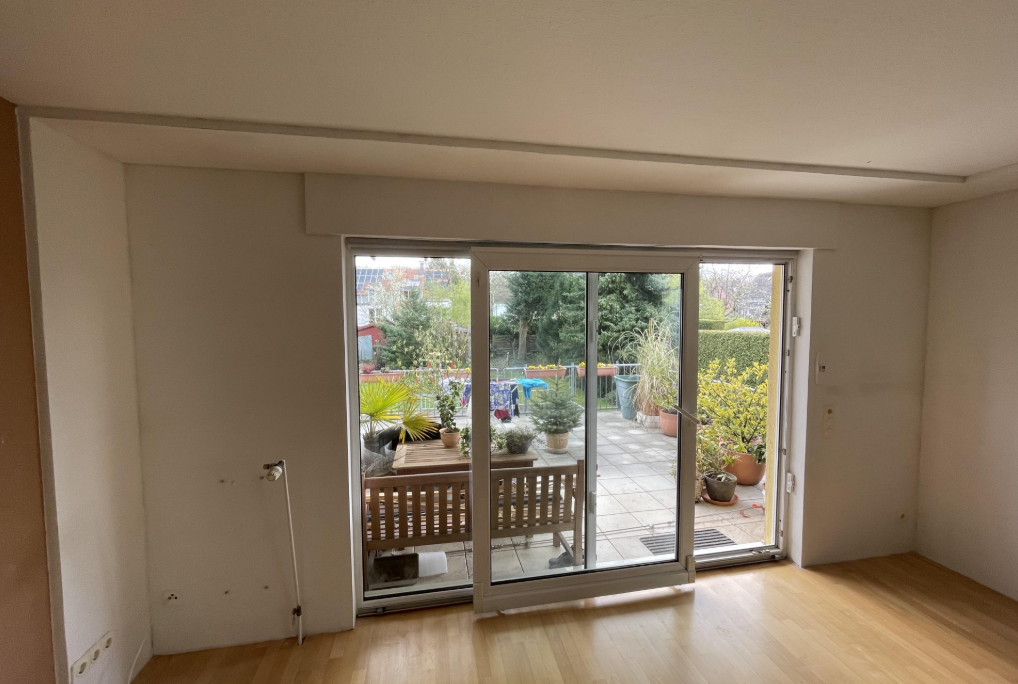 Leerer Wohnraum mit großer Terrassentür und Blick auf bepflanzte Terrasse